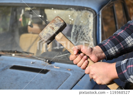 A man is clutching a hammer in front of a bright blue car 119368527