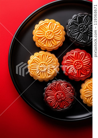 Six colorful mooncakes, including yellow, black, and red, arranged on a black plate with a red backdrop 119368671