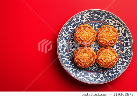 Four mooncakes neatly placed on a blue and white patterned plate, set against a solid red background 119368672