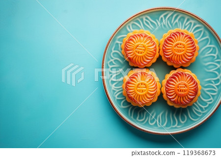 Four bright orange mooncakes with intricate designs on a teal ceramic plate, set on a teal background 119368673