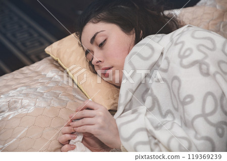 the young girl is bad and she lies on the bed under a blanket with a sad face 119369239