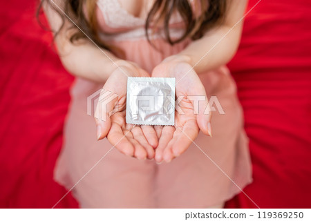 World sexual health day. A woman in her underwear is sitting on the bed and holding a condom package in her hands. The view from the top. The concept of contraception and protection from AIDS World sexual health day. A woman in her underwear is sitting on the bed and holding a condom package in her hands. The view from the top. The concept of contraception and protection from AIDS 119369250