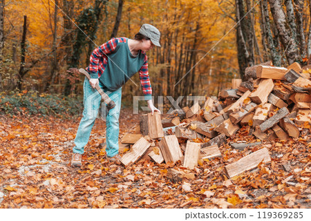 Preparation for the heating season. Young woman chopping wood. In the background autumn forest. Close up Preparation for the heating season. Young woman chopping wood. In the background autumn forest. Close up 119369285