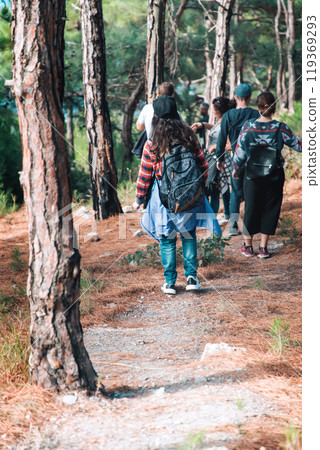 Sports and tourism. A group of people coming down the slope with pine trees. Rear view Sports and tourism. A group of people coming down the slope with pine trees. Rear view 119369293