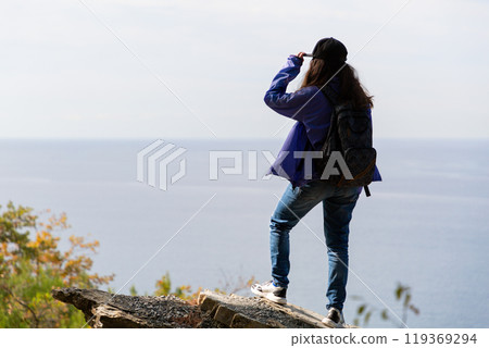 Sports and tourism. A woman with a backpack on her back looks into the distance. In the background, the sea horizon. Rear view 119369294