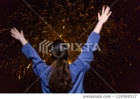 A young woman enjoys the golden fireworks in the sky.Concept of festivals and holidays with fireworks. The view from the back 119369317