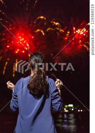 A young woman enjoys the red fireworks in the sky.Concept of festivals and holidays with fireworks. The view from the back A young woman enjoys the red fireworks in the sky.Concept of festivals and holidays with fireworks. The view from the back 119369319