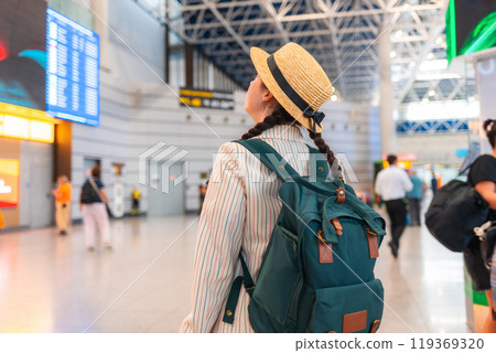 Young Caucasian woman in a straw hat, carrying a backpack, walks through the airport. Rear view, from the back. Traveling by plane, check-in for a flight 119369320