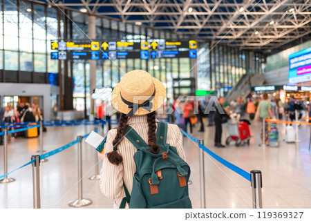 Rear view of Caucasian woman in a straw hat, wearing backpack, walks through the airport. Traveling by plane, check-in for a flight. Concept of vacation Rear view of Caucasian woman in a straw hat, wearing backpack, walks through the airport. Traveling by plane, check-in for a flight. Concept of vacation 119369327