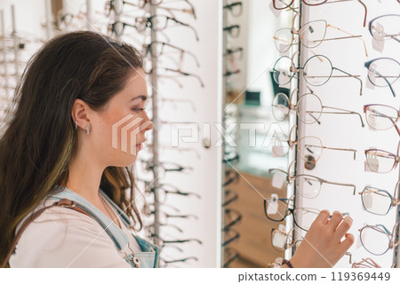 Health and vision. A young and pretty woman chooses glasses in the salon of optics Health and vision. A young and pretty woman chooses glasses in the salon of optics 119369449