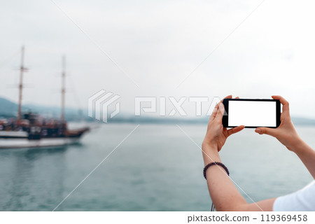 Mock up. The woman holds the phone horizontally. In the background, the sea and ships. Isolate 119369458