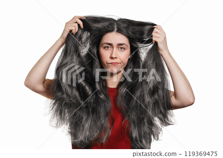 A young disgruntled woman shows off her gray hair. White background. The concept of coloring and hair care A young disgruntled woman shows off her gray hair. White background. The concept of coloring and hair care 119369475