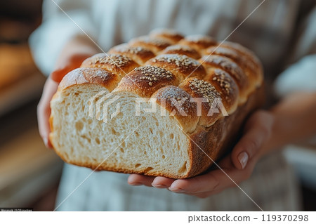 Hands holding a freshly baked golden loaf of bread with sesame seeds and a fluffy interior 119370298