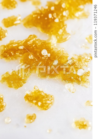 Sticky and shiny cannabis extract crystals spread on a surface 119371246