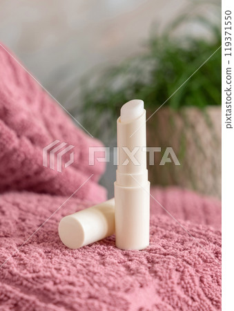 Opened lip balm stick on pink folded towel near green plant in bathroom close up, mockup 119371550