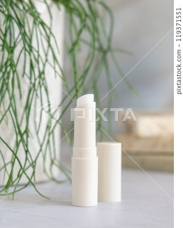 Opened lip balm stick on marble conutertop near potted green plant in bathroom, mockup 119371551