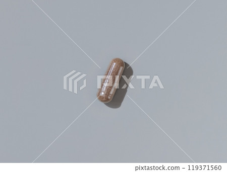 Brown Medical capsule on grey top view, hard shadows. Taking dietary supplements Brown Medical capsule on grey top view, hard shadows. Taking dietary supplements 119371560