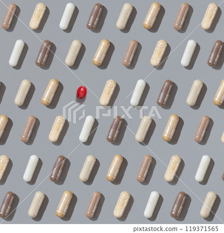 Patern of beige medical capsules with one red on grey top view, hard shadows. Herbal dietary supplements Patern of beige medical capsules with one red on grey top view, hard shadows. Herbal dietary supplements 119371565