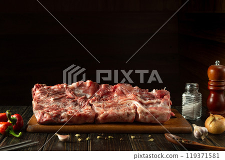 Large piece of meat on a cutting kitchen board. Raw ribs on the kitchen table. Space on a black background for a recipe or menu Large piece of meat on a cutting kitchen board. Raw ribs on the kitchen table. Space on a black background for a recipe or menu 119371581