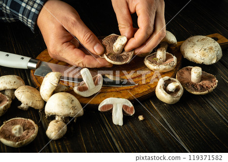 Chef sorts Agaricus mushrooms by hand to prepare delicious food. Set of champignon mushrooms on an antique kitchen table. Delicious recipe for dinner Chef sorts Agaricus mushrooms by hand to prepare delicious food. Set of champignon mushrooms on an antique kitchen table. Delicious recipe for dinner 119371582
