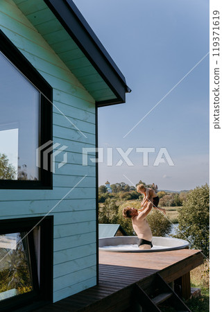 Father and son bonding in an outdoor hot tub with scenic views, enjoying playful moments in the sun Father and son bonding in an outdoor hot tub with scenic views, enjoying playful moments in the sun 119371619