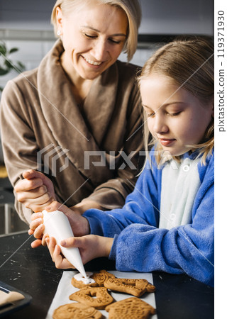 Mother and daughter decorating Christmas cookies together, holiday baking tradition, festive kitchen, family bonding, Christmas countdown, creating holiday magic. 119371930