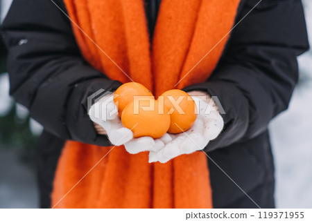Close-up of woman holding an orange in a snowy outdoor scene. Winter immunity, fresh citrus, healthy living during cold season Close-up of woman holding an orange in a snowy outdoor scene. Winter immunity, fresh citrus, healthy living during cold season 119371955