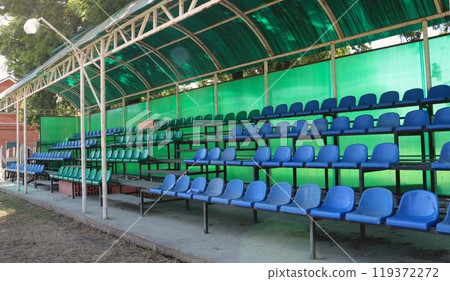 blue and green plastic chairs under a green canopy, a fragment of an open-air spectator stand without visitors, places for watching horse races at a provincial hippodrome blue and green plastic chairs under a green canopy, a fragment of an open-air spectator stand without visitors, places for watching horse races at a provincial hippodrome 119372272