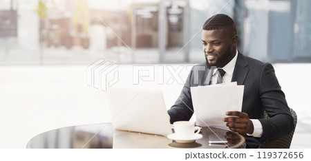Confident African Entrepreneur Sitting At Laptop Working With Papers Sitting In Cafe Outside. Business Lifestyle. Free Space 119372656