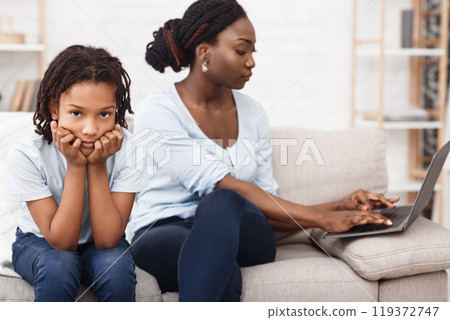 No Time For Child. African mom is busy working at home on laptop, sad bored daughter nearby. Free space No Time For Child. African mom is busy working at home on laptop, sad bored daughter nearby. Free space 119372747