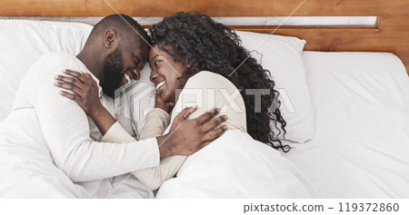 Lovely morning. Black millennial couple cuddling in bed at home, resting, and enjoying weekend together 119372860