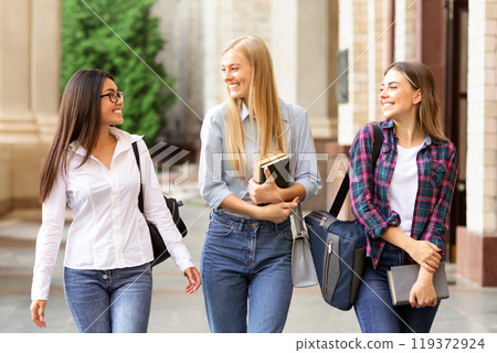 Female students walking out of college building and chatting during break 119372924