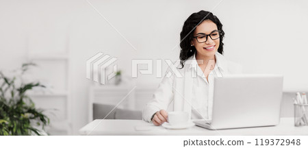Assistant. Portrait of happy mexican woman in glasses working on laptop, drinking coffee, copyspace 119372948