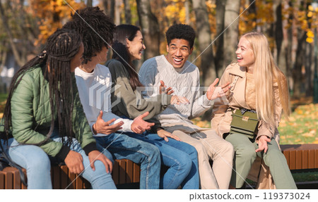 Black cheerful guy telling his multiracial friends funny story, spending time together in public park 119373024