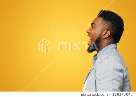 Amazed african american man shouting at free space with excitement, yellow studio background, side view Amazed african american man shouting at free space with excitement, yellow studio background, side view 119373043