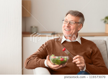 Smiling Senior Gentleman Enjoying Vegetable Salad Sitting On Couch Indoor. Healthy Eating In Old Age. Empty Space, Selective Focus 119373070