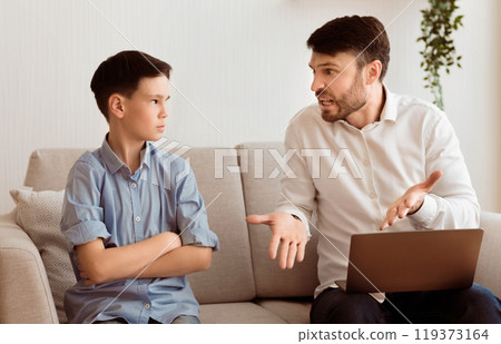 Generations Misunderstanding. Irritated Dad Yelling At Offended Son Working On Laptop Sitting On Sofa Indoor. Selective Focus 119373164