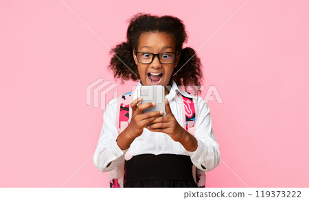 Excited Black Schoolgirl Using Smartphone On Yellow Studio Background. Kids And Phone Addiction. Free Space 119373222