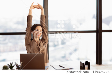 Stretching At Workplace. Happy beautiful young woman sitting at desk in modern office, looking away, copyspace 119373228