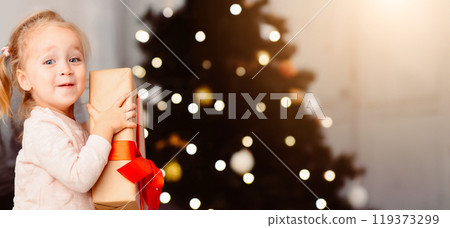 Big Christmas gift. Adorable toddler holding present box near xmas tree, free space Big Christmas gift. Adorable toddler holding present box near xmas tree, free space 119373299