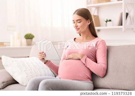 Content Pregnant Woman Using Digital Tablet Computer Reading E-Book Relaxing Sitting On Couch At Home 119373328