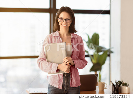 Confident Manager. Smiling female office worker wearing specs holding folder, looking at camera, copyspace 119373334