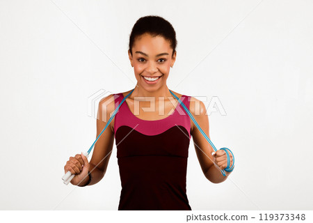 Fitness And Sport. Happy Afro Girl Holding Jump Rope Smiling At Camera Standing On White Background. Studio Shot, Isolated Fitness And Sport. Happy Afro Girl Holding Jump Rope Smiling At Camera Standing On White Background. Studio Shot, Isolated 119373348