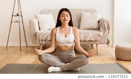 Morning Fitness. Teen Girl Meditating On Mat At Home, Sitting In Lotus Pose Morning Fitness. Teen Girl Meditating On Mat At Home, Sitting In Lotus Pose 119373352