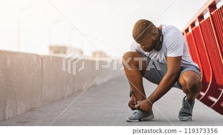 Black man tying running shoes on bridge, free space 119373356