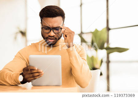 Bad News. Focused african american man looking at digital tablet at workplace, touching glasses, copyspace 119373369