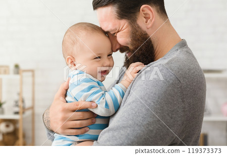 Cheerful father and son cuddling at home, enjoying time together Cheerful father and son cuddling at home, enjoying time together 119373373