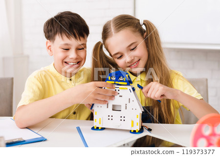 Two children, a boy and a girl, are working together to build a robot toy. They are both smiling and seem to be enjoying the activity. The robot is made of plastic and has blue and yellow details 119373377
