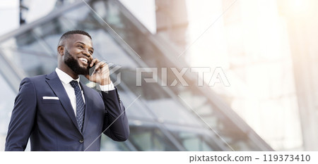 Happy African Entrepreneur Talking On Mobile Phone Standing In Urban Area In City. Business Communication Strategies Concept. Empty Space Happy African Entrepreneur Talking On Mobile Phone Standing In Urban Area In City. Business Communication Strategies Concept. Empty Space 119373410