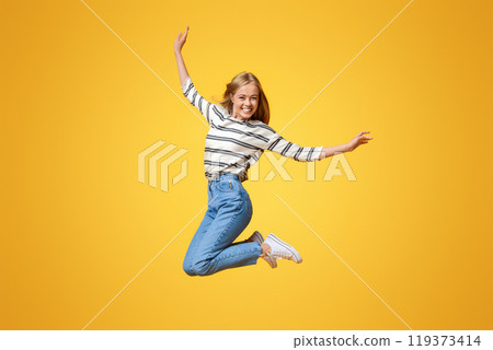 Happy teenage girl jumping in the air, pretending she is flying. Orange studio background with free space 119373414